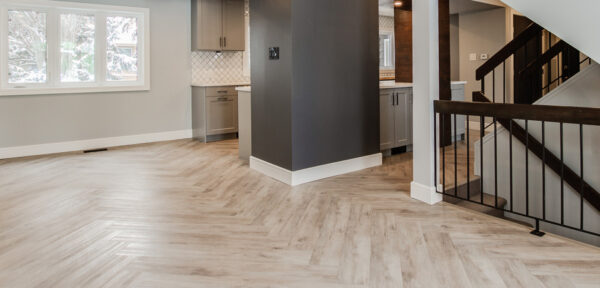 Bright and spacious interior of a modern home featuring a herringbone patterned floor, kitchen area, and a staircase
